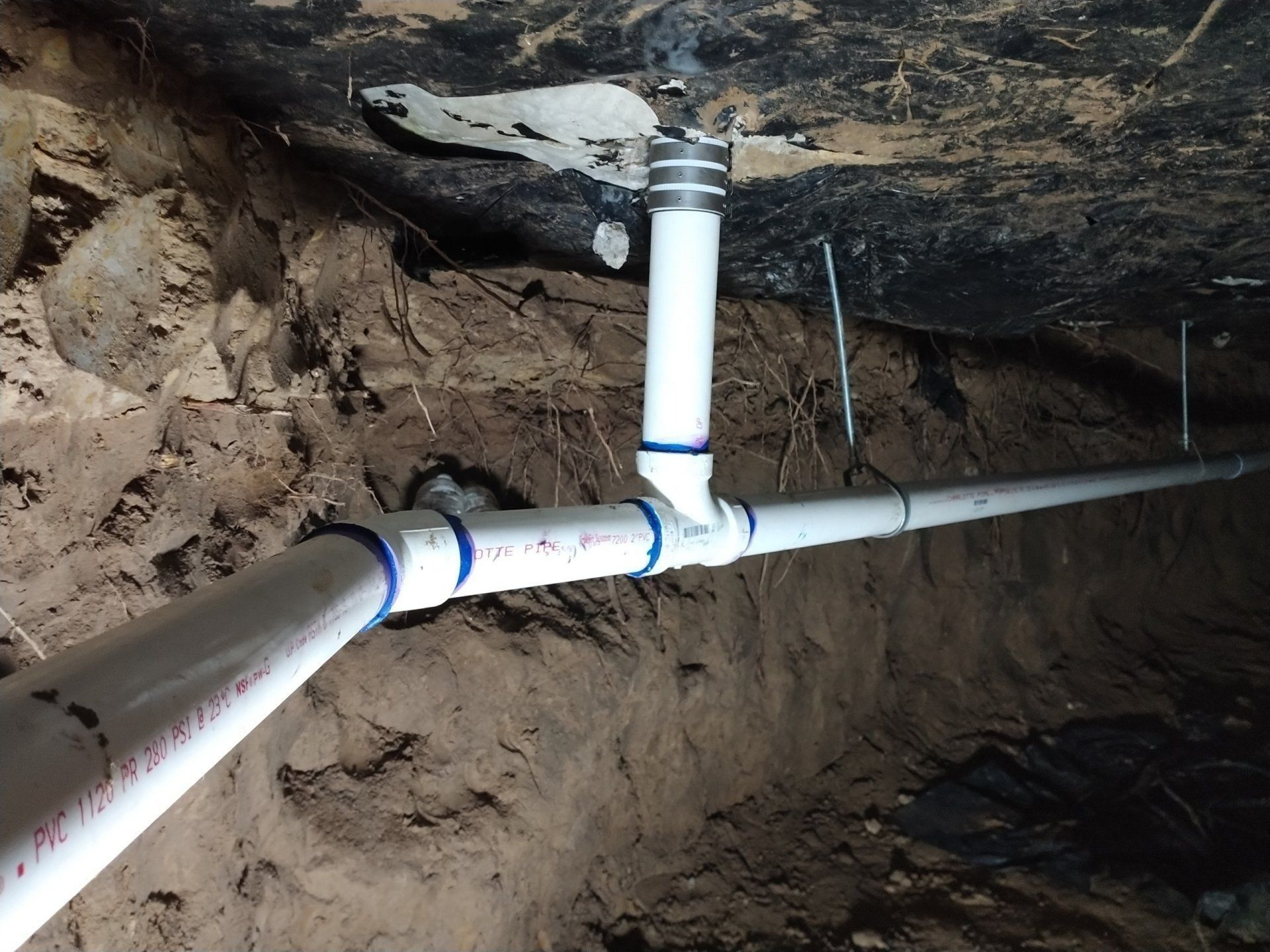 White PVC pipes connected in a rocky dirt trench underground