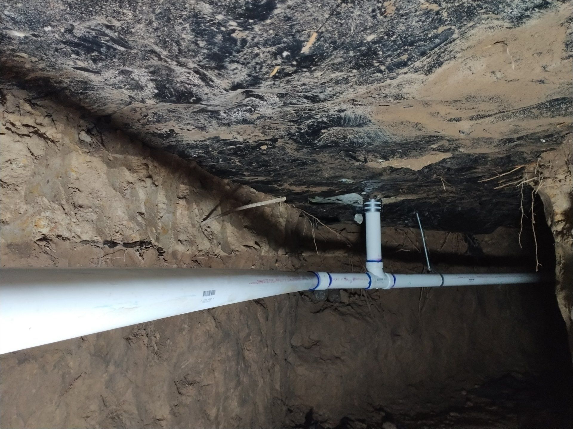 White pipe running through a rocky underground tunnel with rough cave ceiling and walls