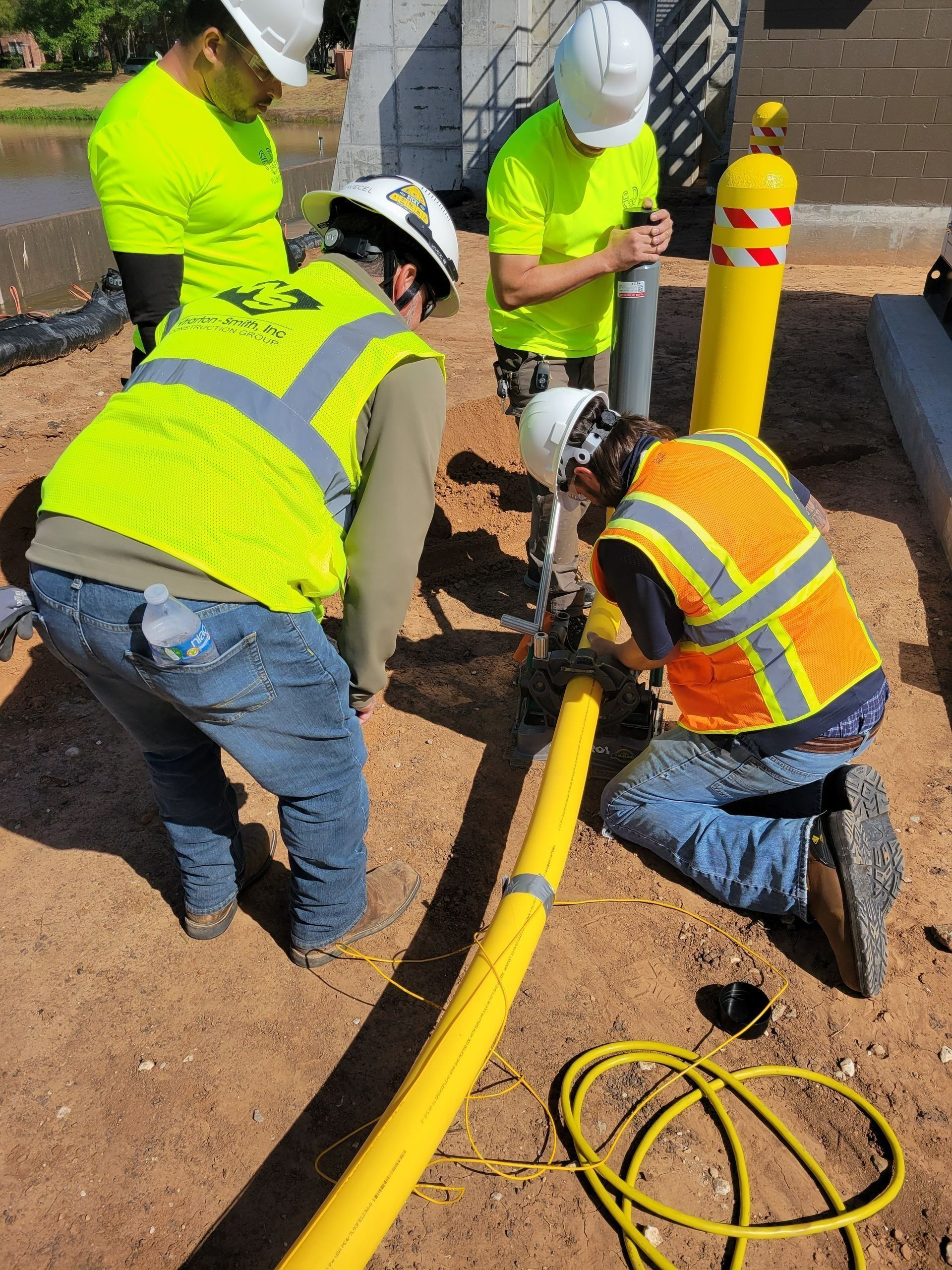 Workers in reflective vests install a yellow utility cable near a roadside trench.