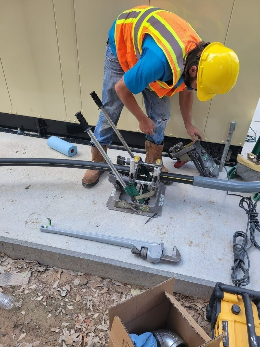 Worker in yellow hard hat and safety vest using a power tool on a concrete slab at a construction site.