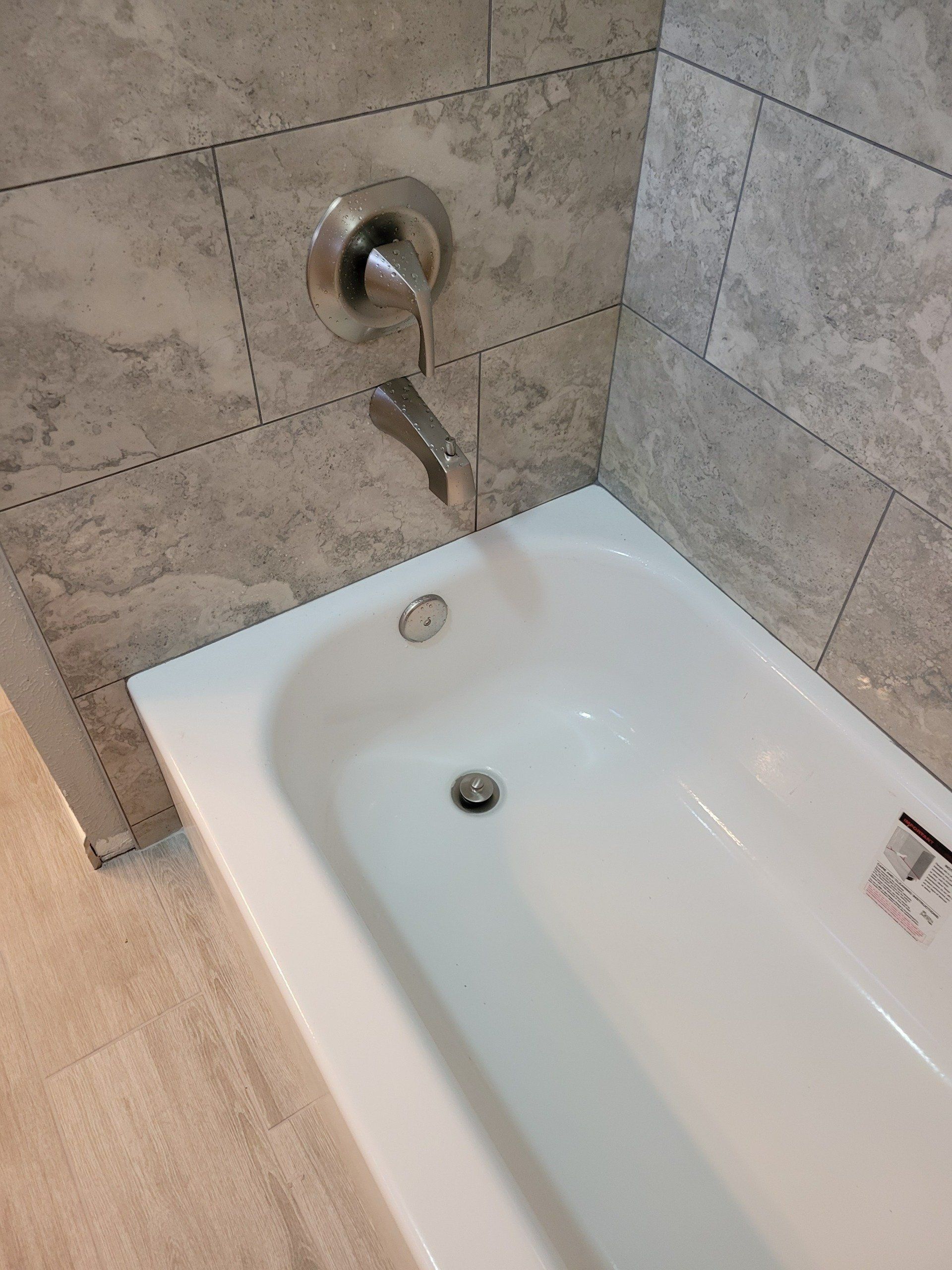 Bathtub with wall-mounted shower faucet and beige tiled walls in a bathroom