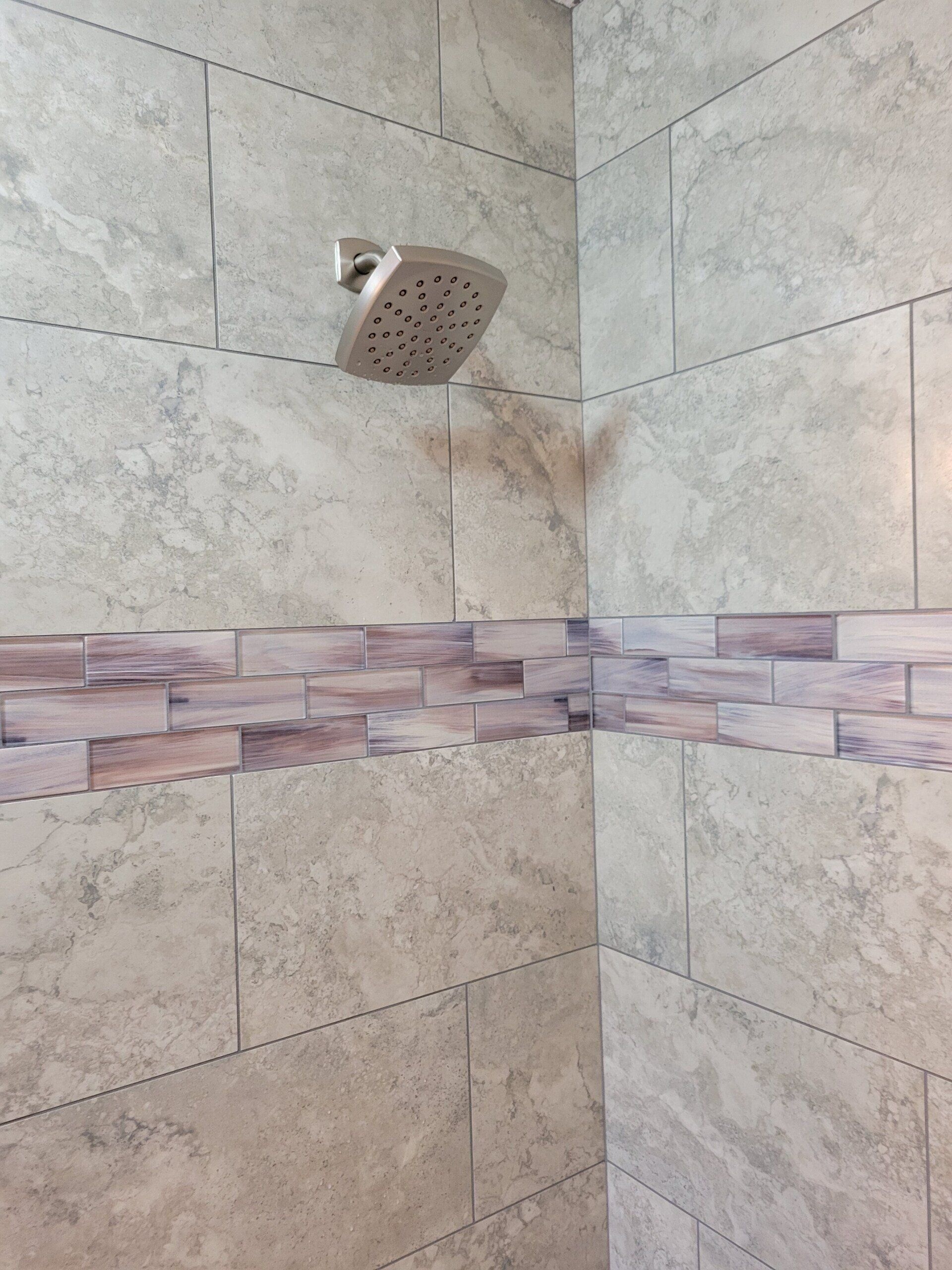 Corner shower with beige tile walls, a decorative tile band, and a chrome showerhead.