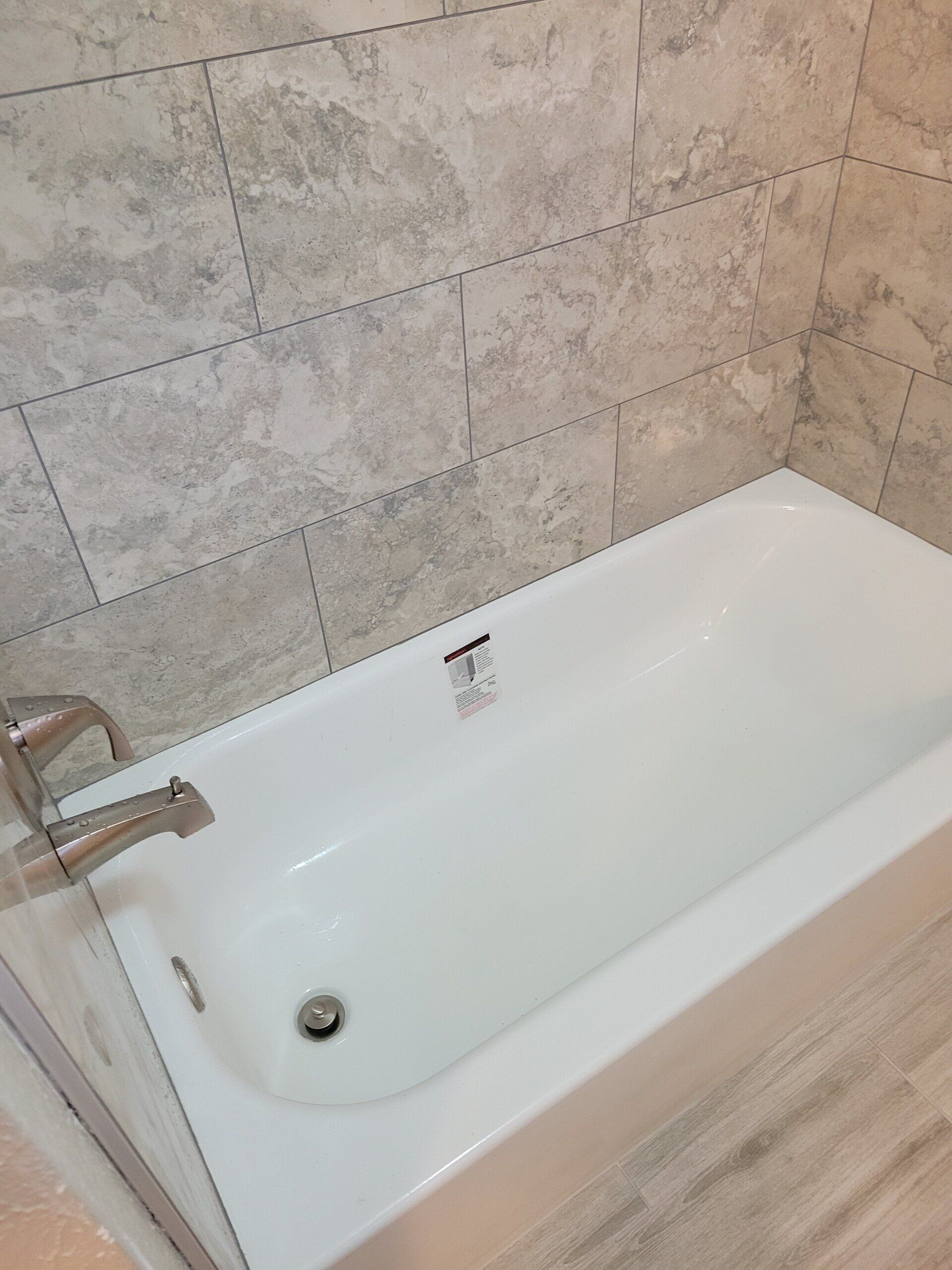 White bathtub with chrome faucet against beige tiled bathroom wall.