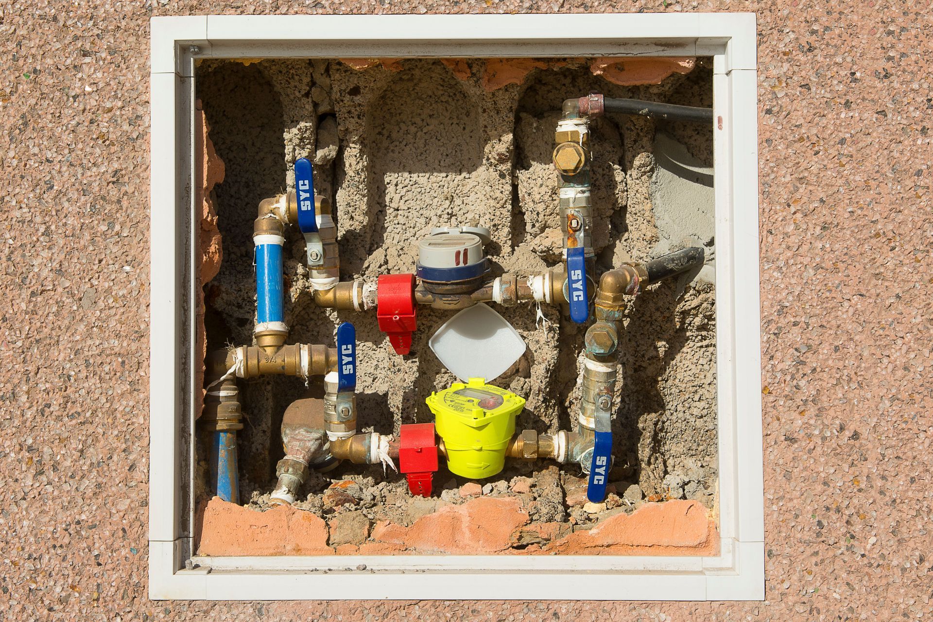 Utility meter box with pipes and valves behind a small access panel