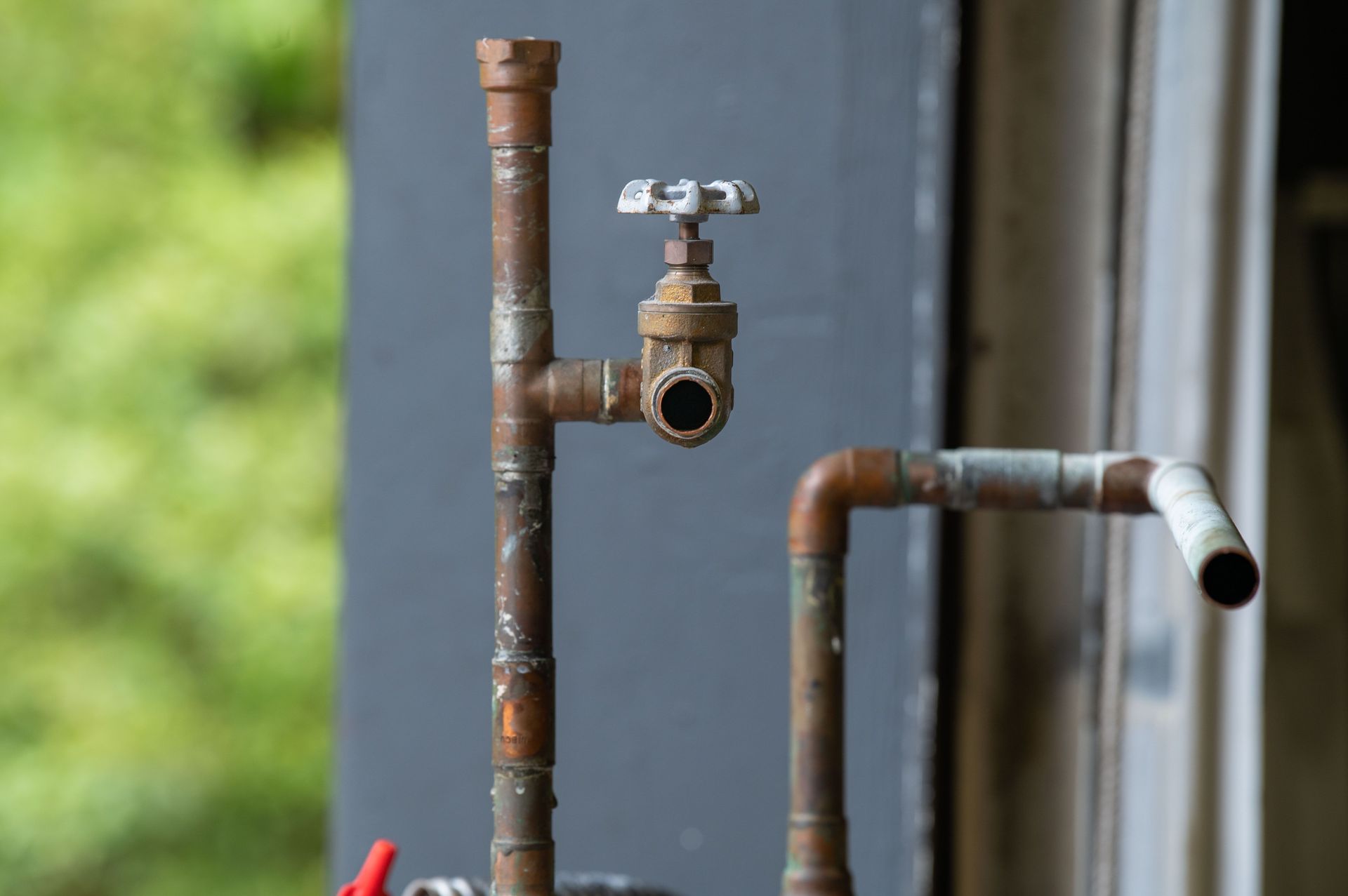 Rusty outdoor pipes with a metal faucet and a white-capped open pipe end