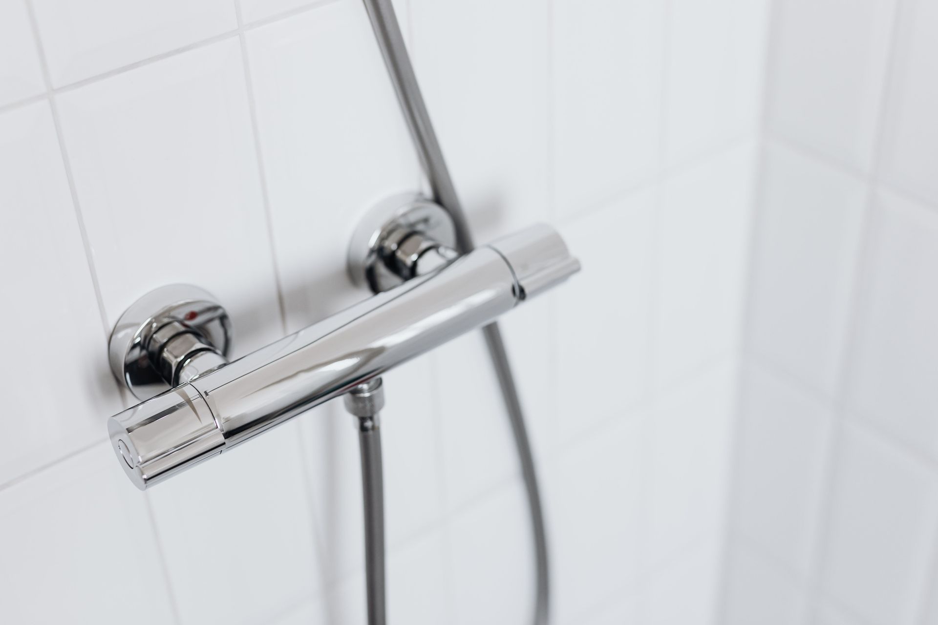 Chrome shower faucet and handheld shower hose on white tiled bathroom wall