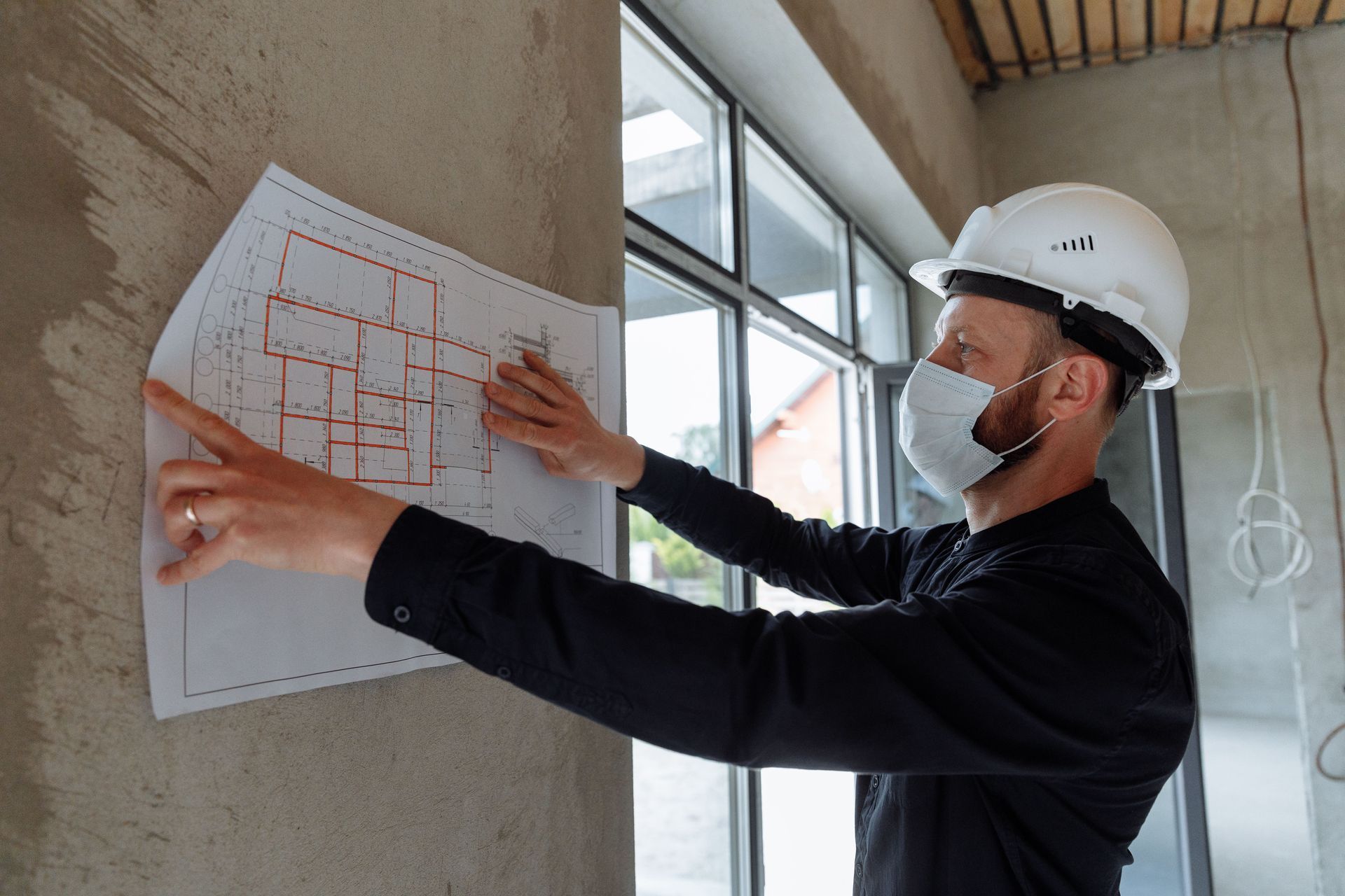 Architect in hard hat reviewing blueprint on a wall inside a building under construction