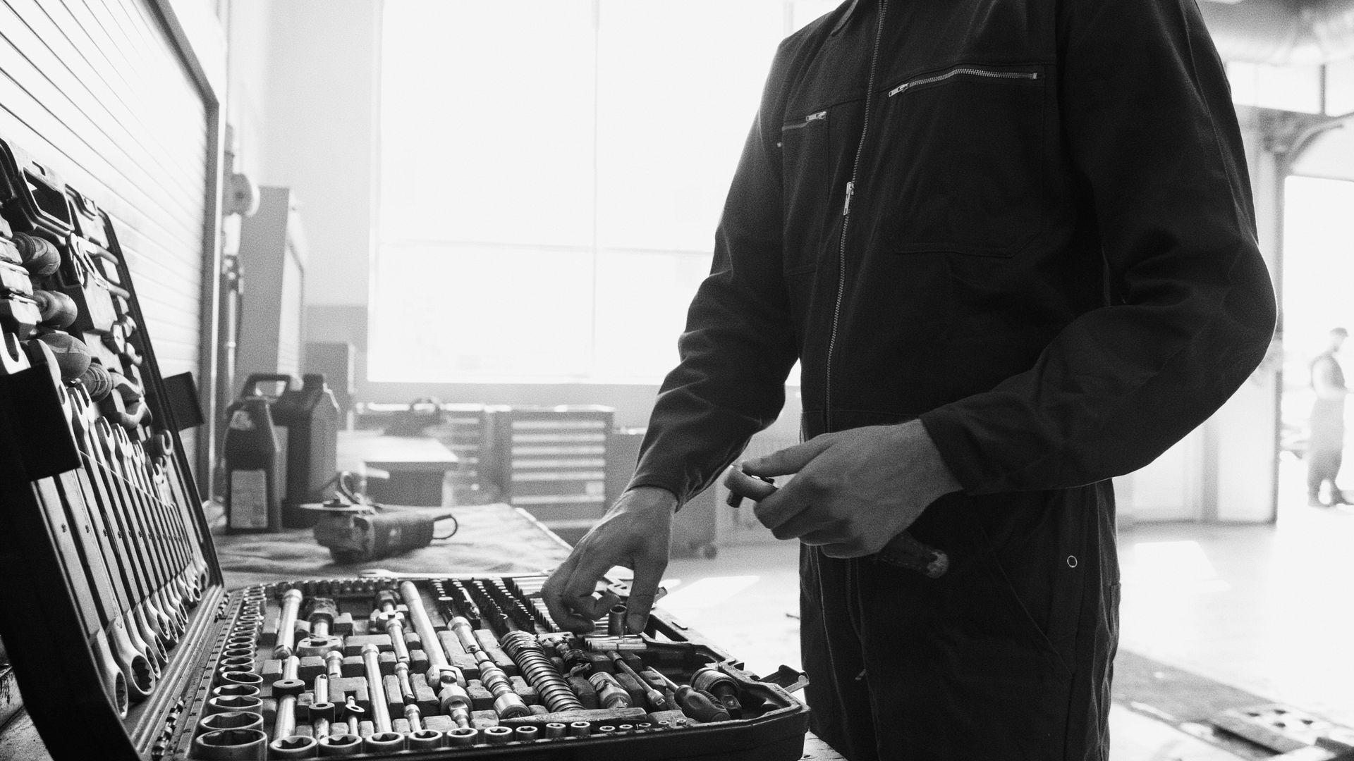 Person in dark jacket arranging tools on a workbench in a bright workshop