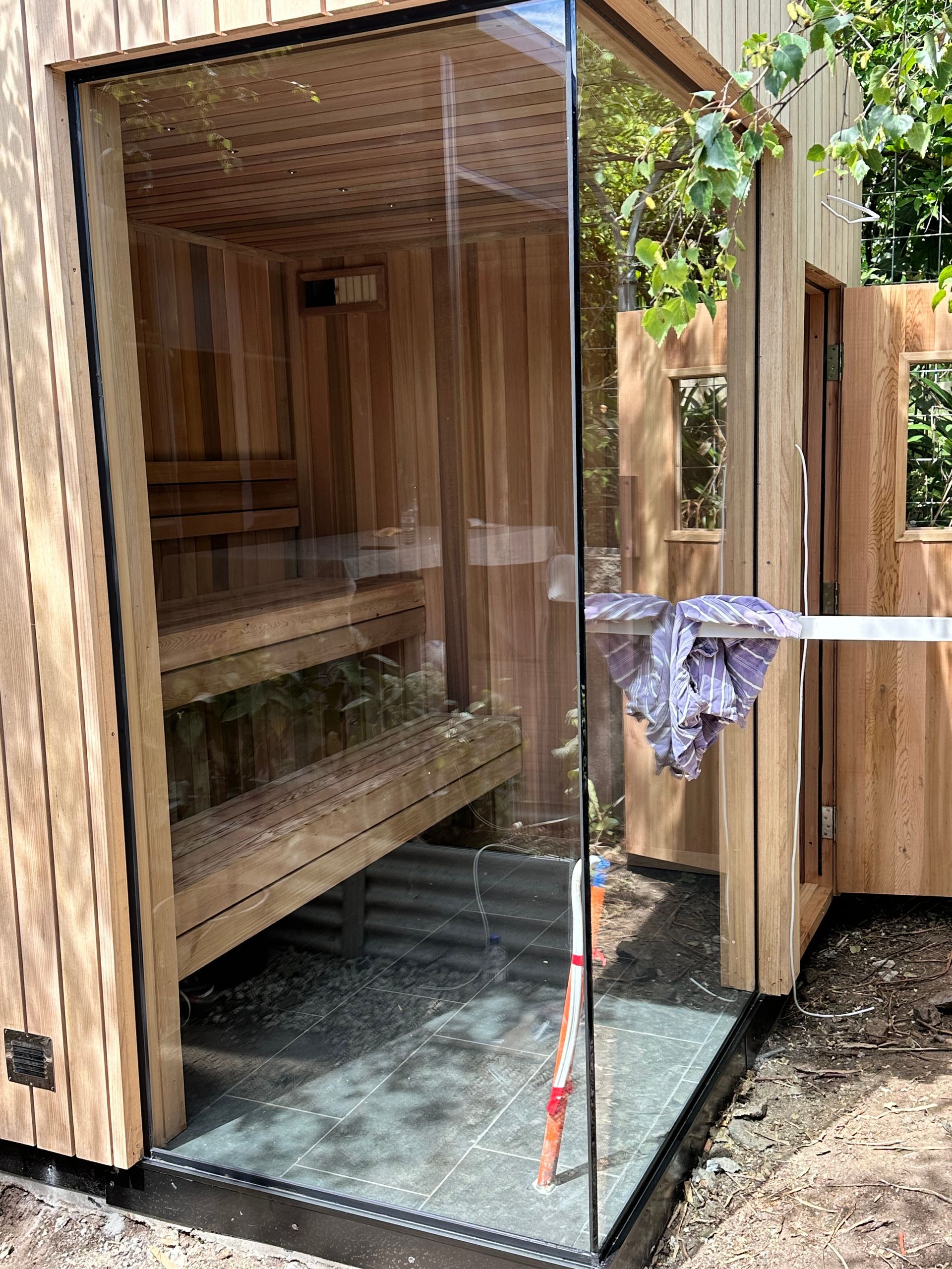 A wooden sauna with a glass door and a mop.