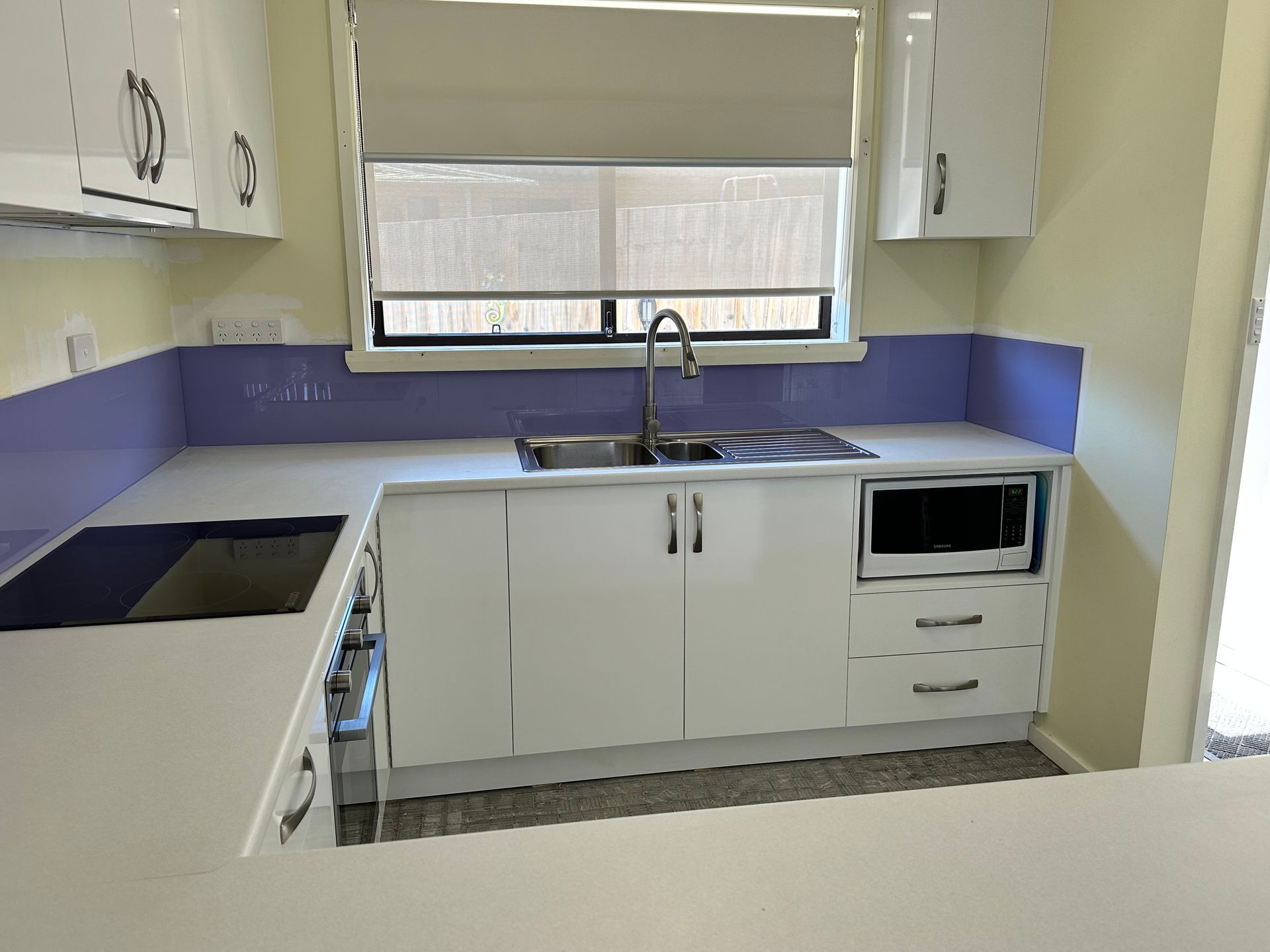A kitchen with white cabinets , a sink , a microwave , and a window.