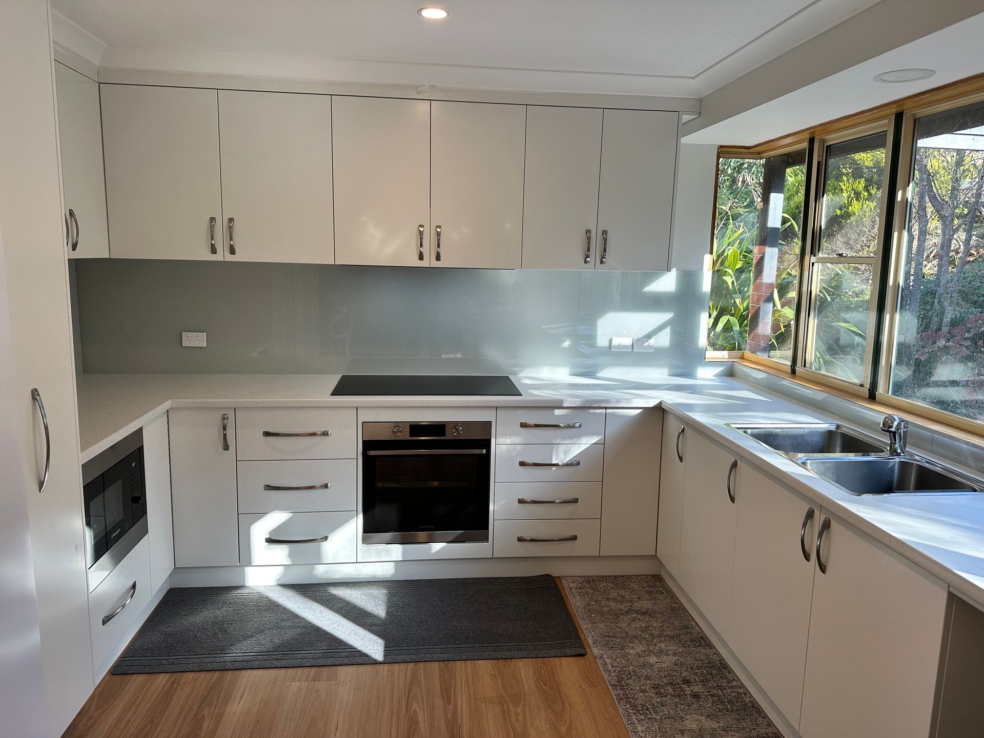 A kitchen with white cabinets , a stove , a sink , and a window.