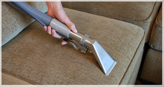 A person is cleaning a couch with a vacuum cleaner.