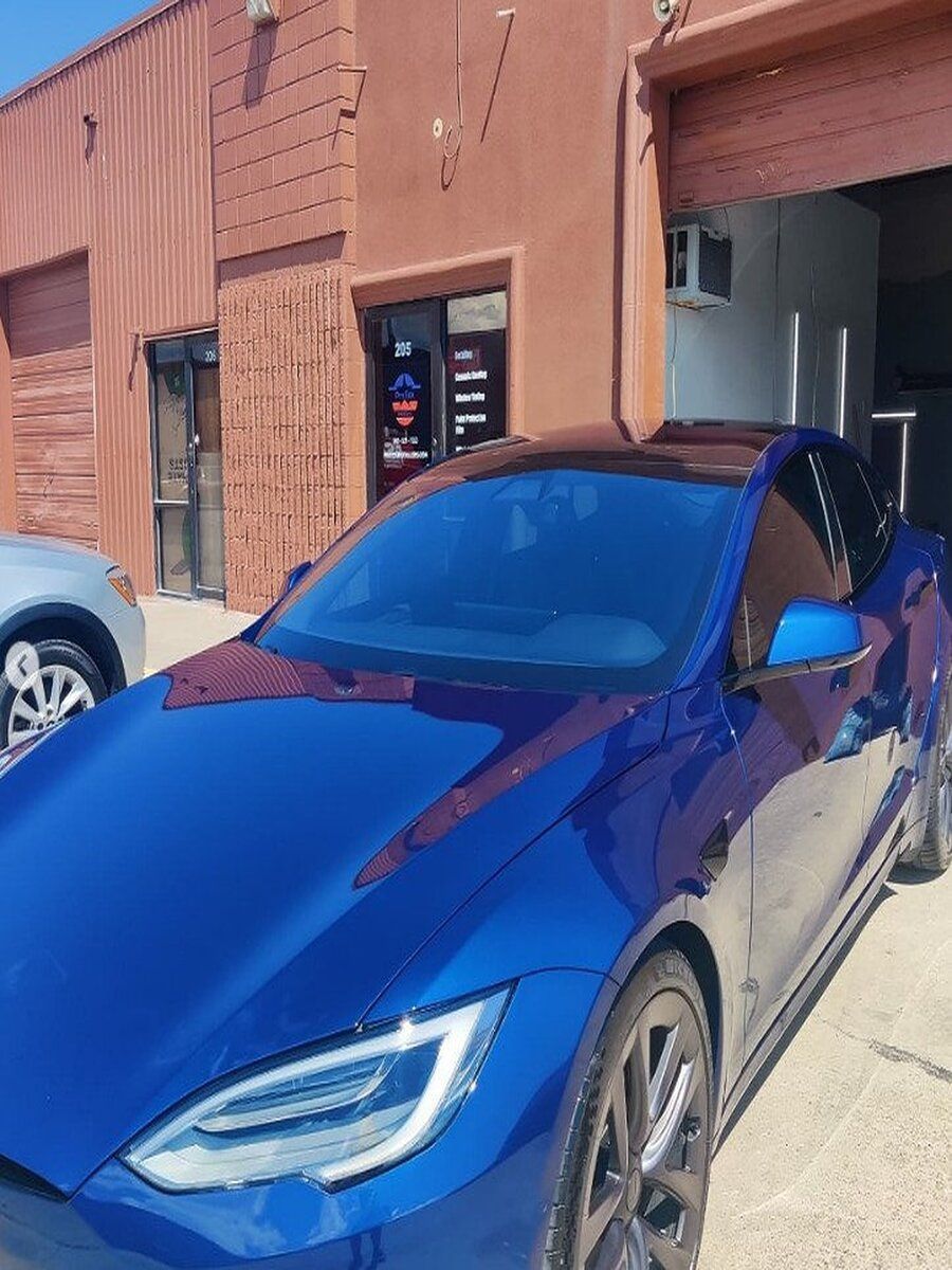 A blue tesla model s is parked in front of a building.