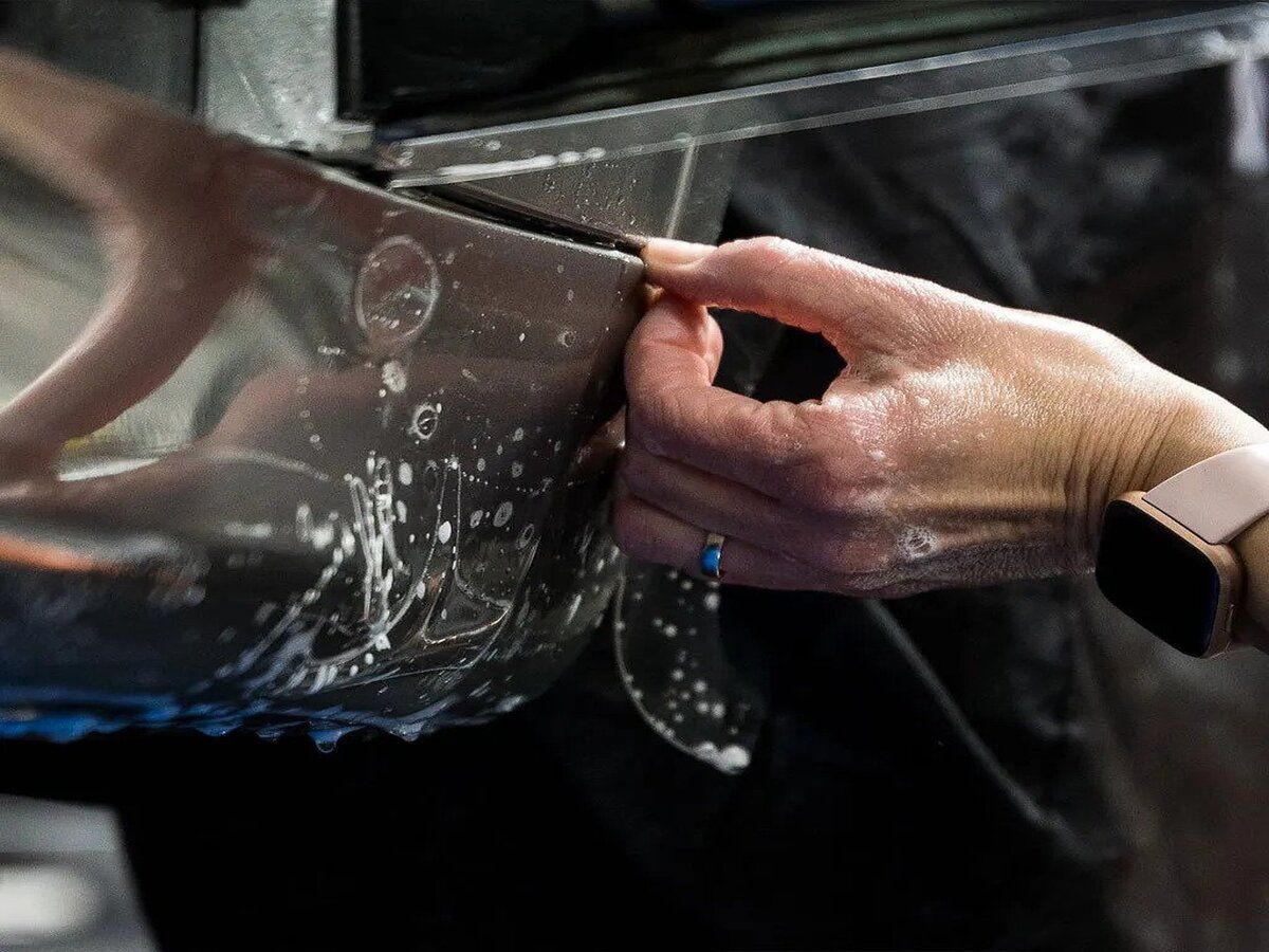 A person is applying a protective film to the side of a car.