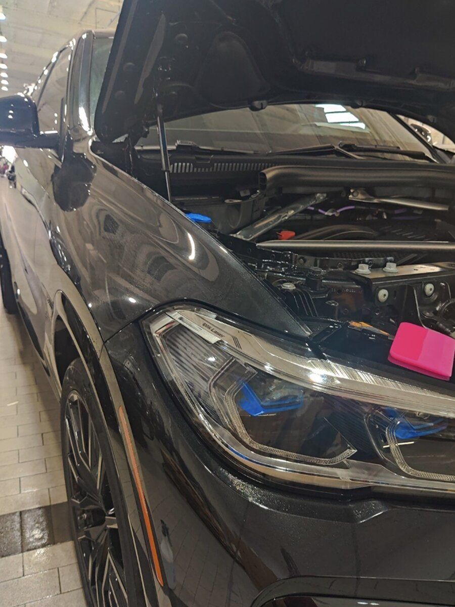 a black car with the hood up is parked in a garage .