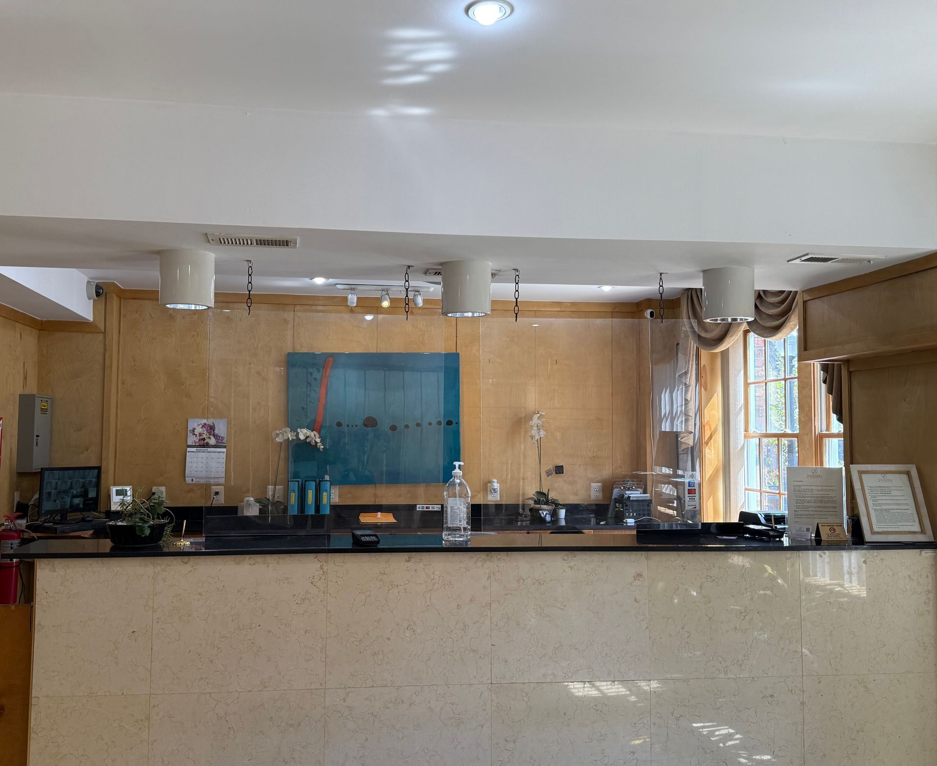 Hotel front desk with marble counter, glass partition, and tan backdrop.