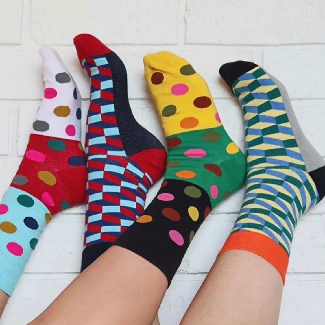 Four Colourful Patterned Socks on Legs Against a White Brick Wall — Decadence Gifts & Homewares in Emerald, QLD