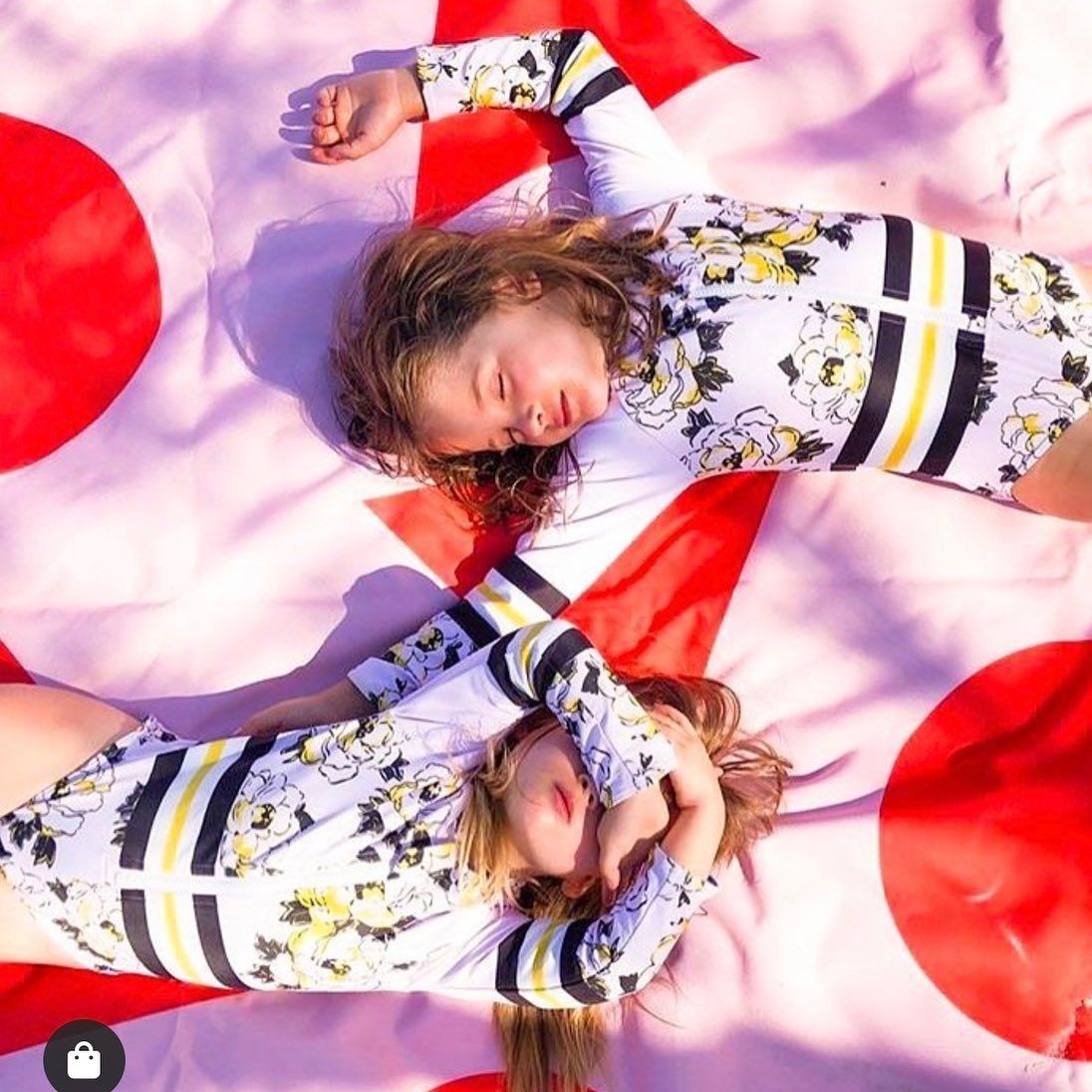 Two Children in Floral Print Swimwear Lying on a Pink and Red Spotted Blanket — Decadence Gifts & Homewares in Yeppoon, QLD