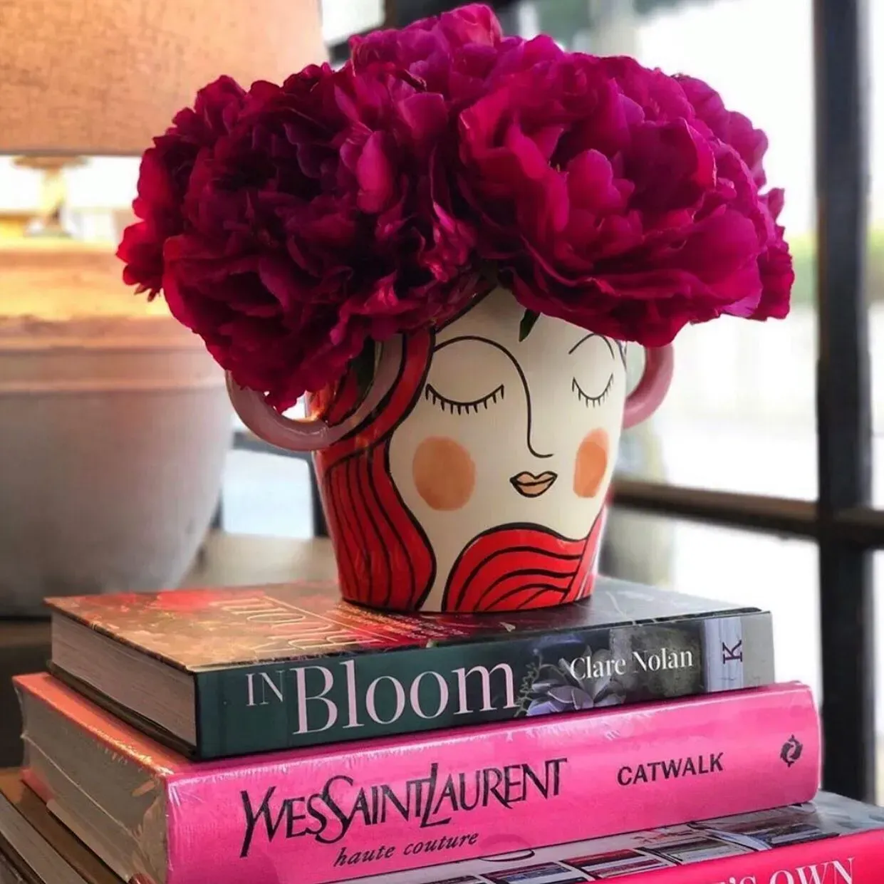 Floral Arrangement in a Face-shaped Vase Atop Books With Pink Covers — Decadence Gifts & Homewares in Springsure, QLD