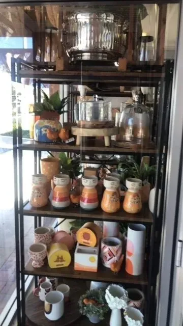 A metal and wood shelf displays various kitchenware and plants, including pots, jars, and stainless steel cookware.