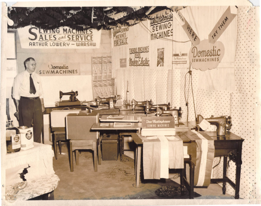 Sepia-toned vintage shop interior with sewing machines, tables, and advertising signs on the walls