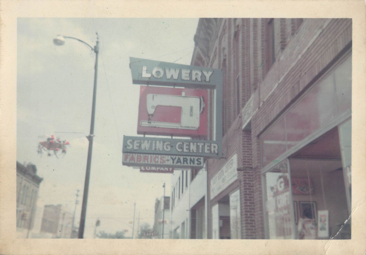 Vintage street sign for Lowery Sewing Center and yarns hanging on a city building facade