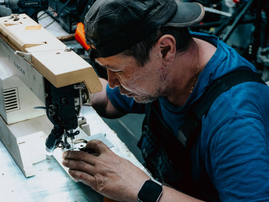 Man using a sewing machine in a workshop, focused on stitching fabric by hand and machine