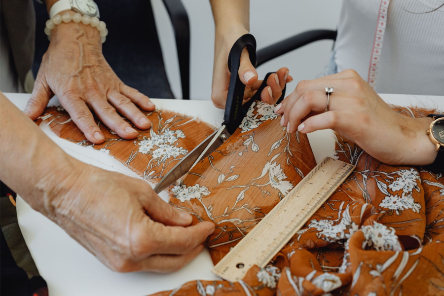 Hands using scissors and a ruler to cut orange fabric covered in white shavings.