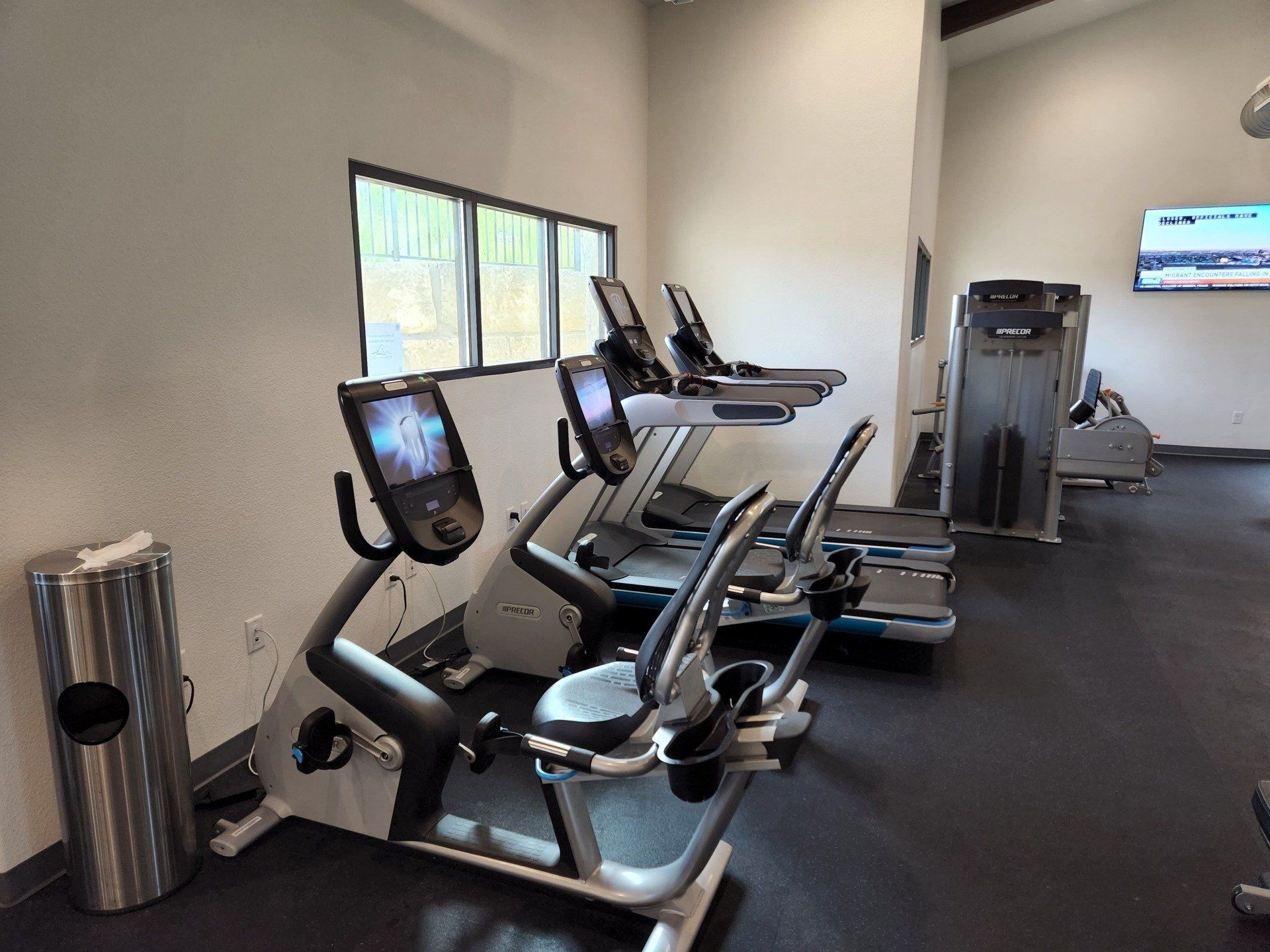 A fitness room with two exercise bikes in the foreground and two treadmills in the background, near a wall-mounted TV.