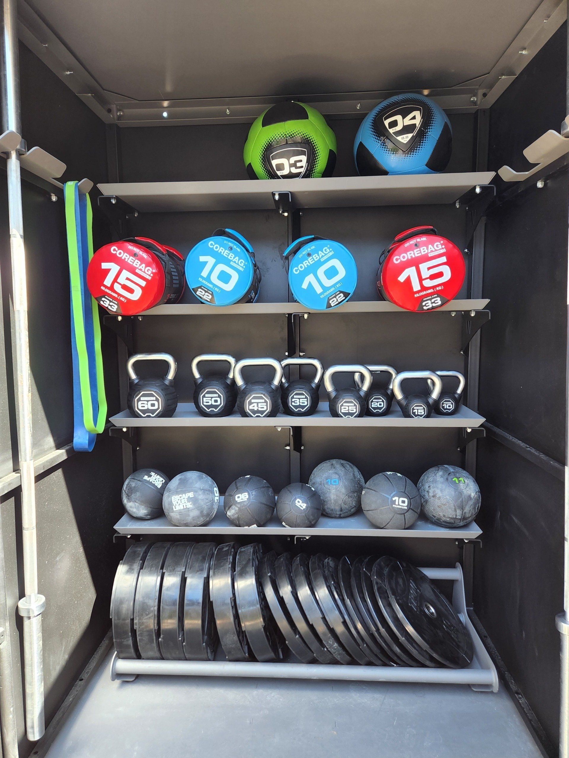 A storage rack containing medicine balls, kettlebells, slam balls, and weight plates organized on shelves.