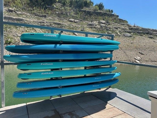 A stack of seven blue paddleboards stored on a rack on a dock overlooking a lake.