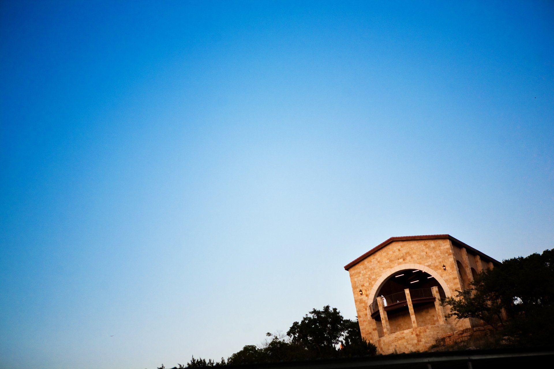 A stone building with a large arched entrance stands on a hill against a clear, deep blue sky.