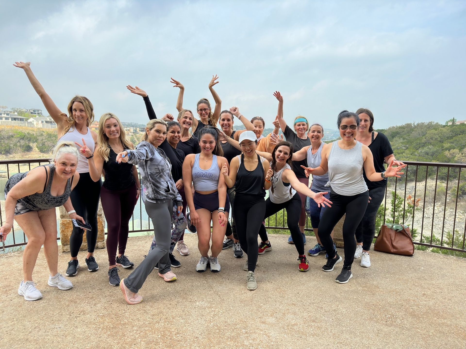 A diverse group of people in athletic wear pose together outdoors on a scenic stone overlook on a cloudy day.