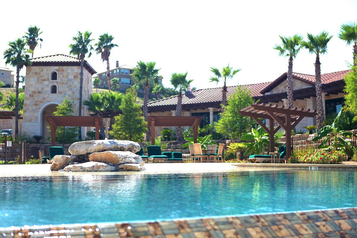 A resort-style swimming pool with a stone rock feature in front of a building with a tower and palm trees.