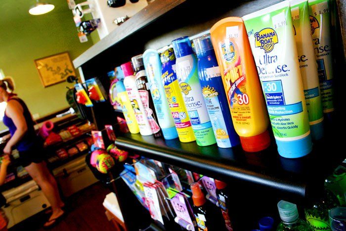 A shelf in a store stocked with rows of various colorful sunscreen bottles, with a person standing in the background.