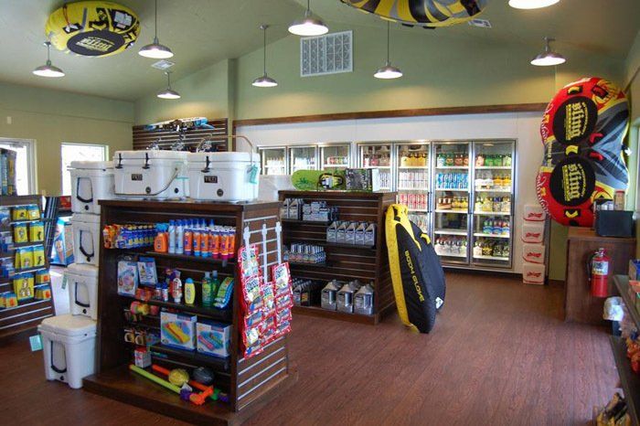 Retail shop interior with shelves of supplies, coolers, beverage refrigerators, and inflatable tubes hanging from ceiling.