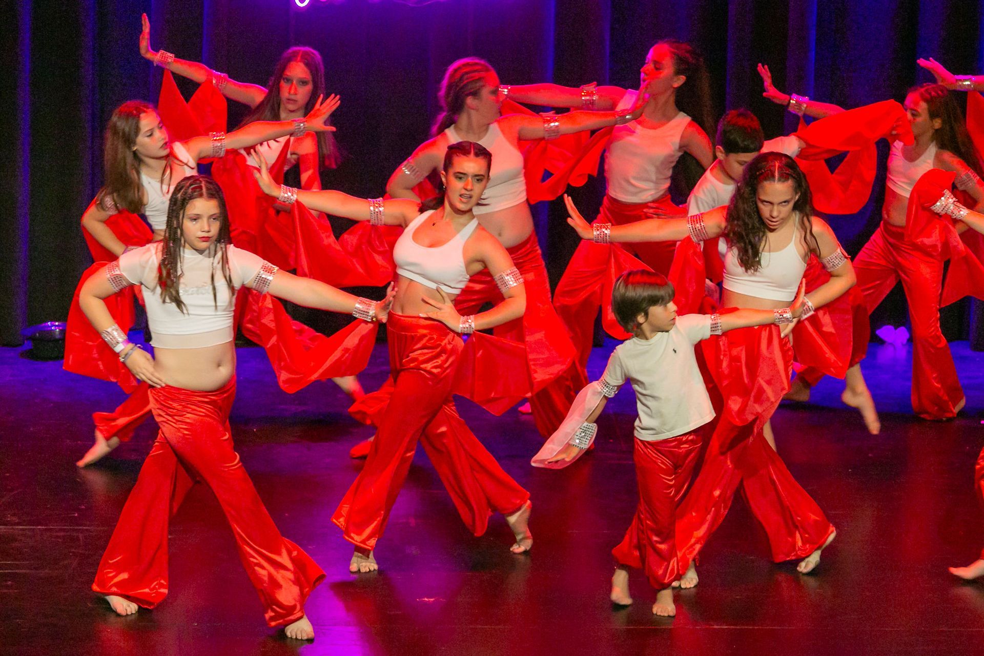 En el escenario actúan bailarines con pantalones y camisetas rojas; muchos de ellos tienen los brazos extendidos.