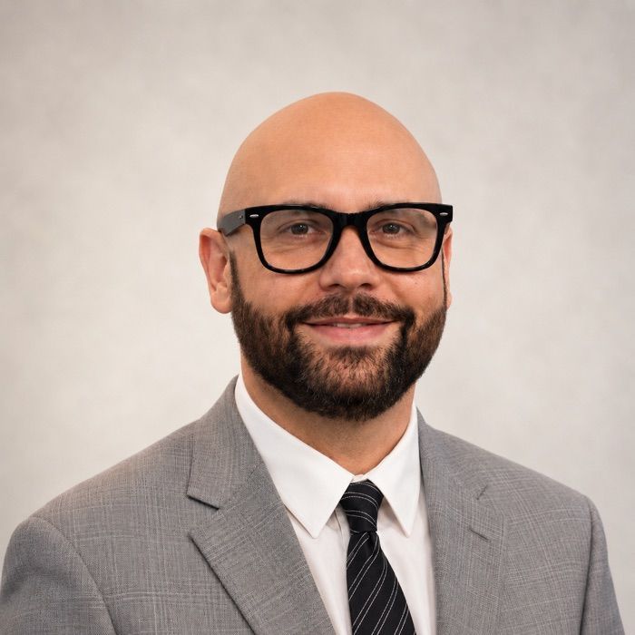 Portrait of a smiling man in glasses and a gray suit against a plain light background