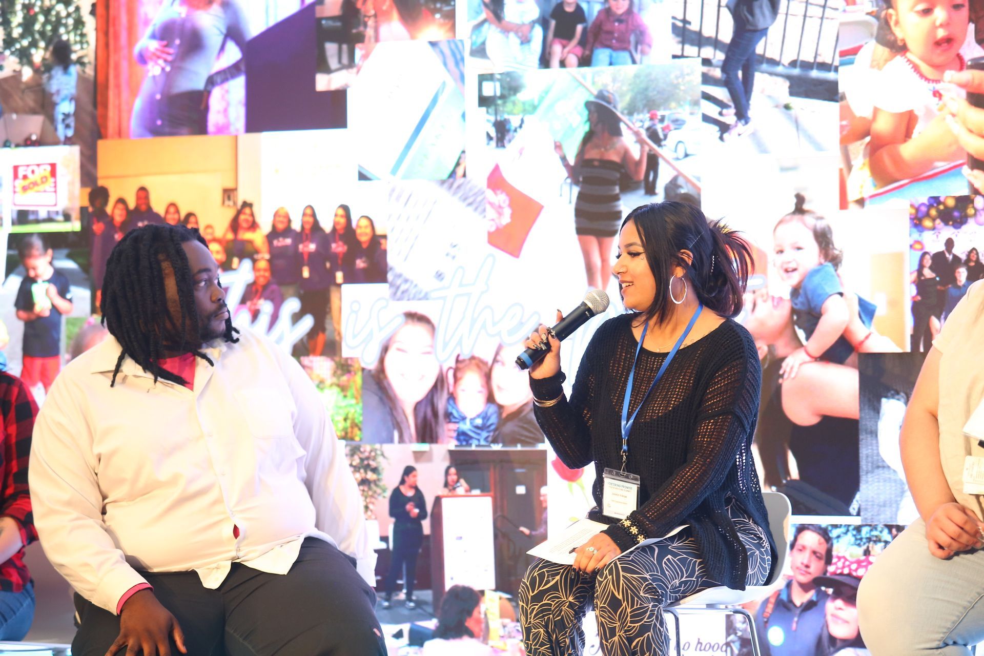 Two people seated on a stage in front of a collage backdrop, one speaking into a microphone.