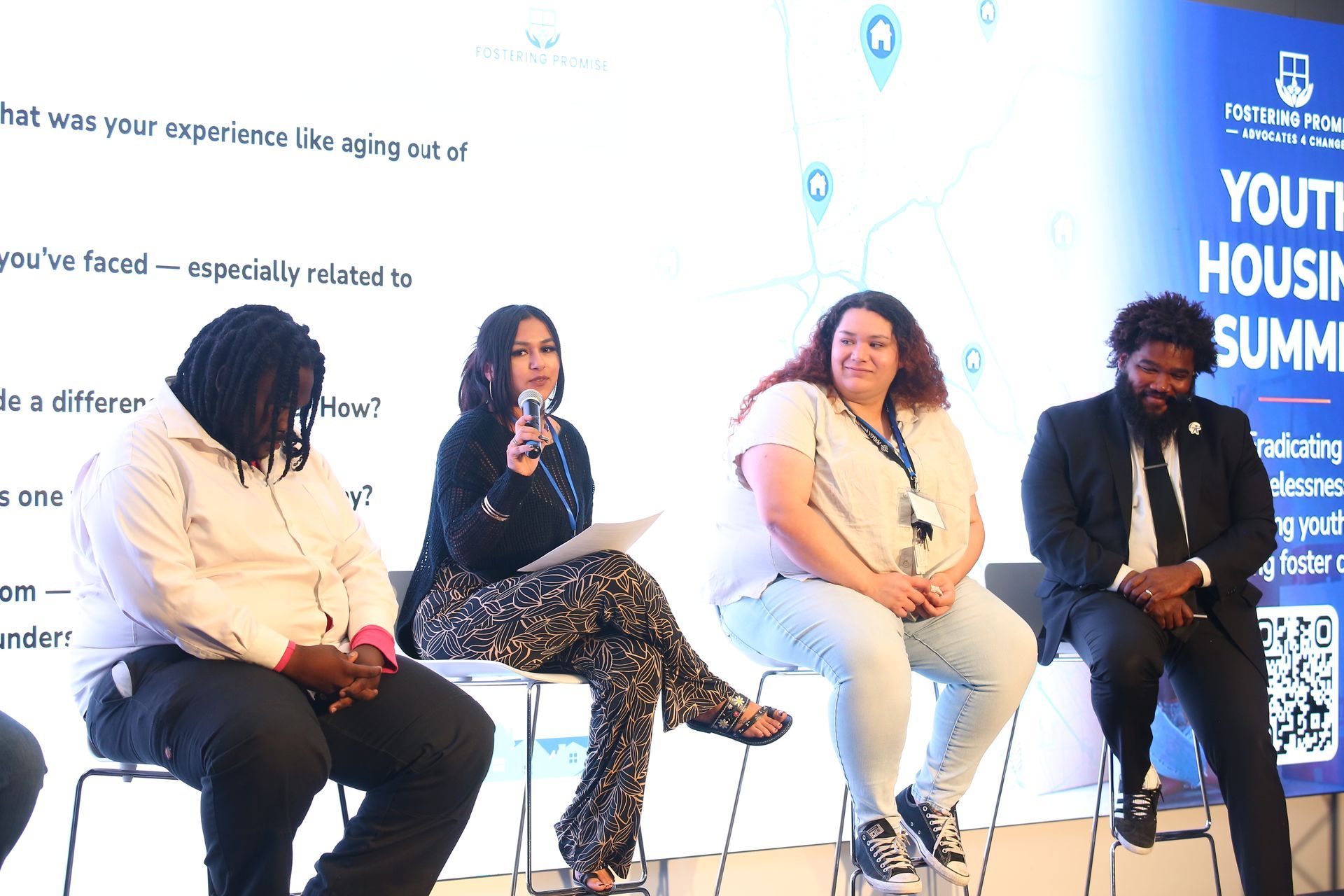 Four people seated on stage during a panel discussion, with a branded event backdrop behind them.