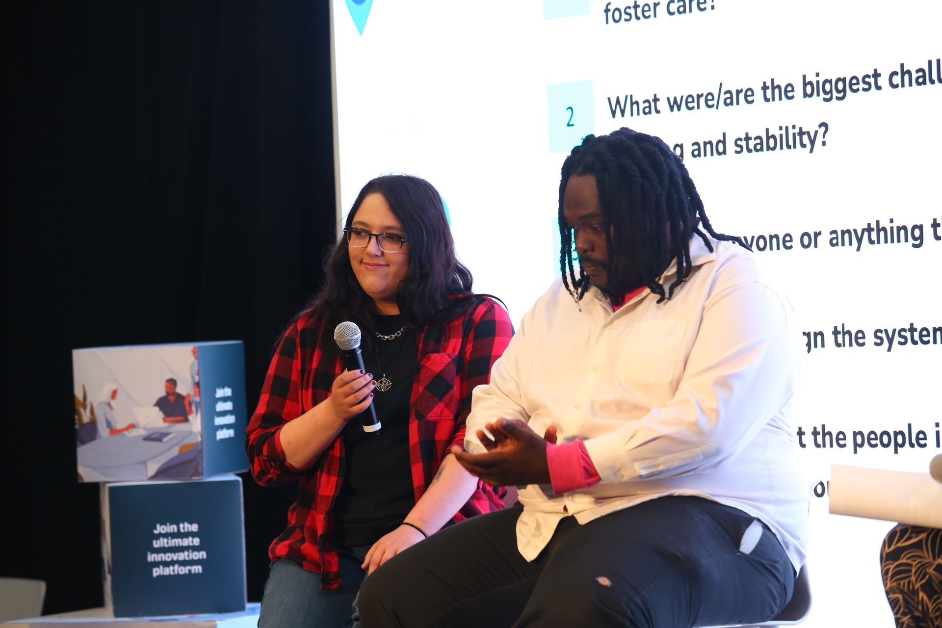 Two women seated onstage, smiling and speaking into microphones during a panel discussion.