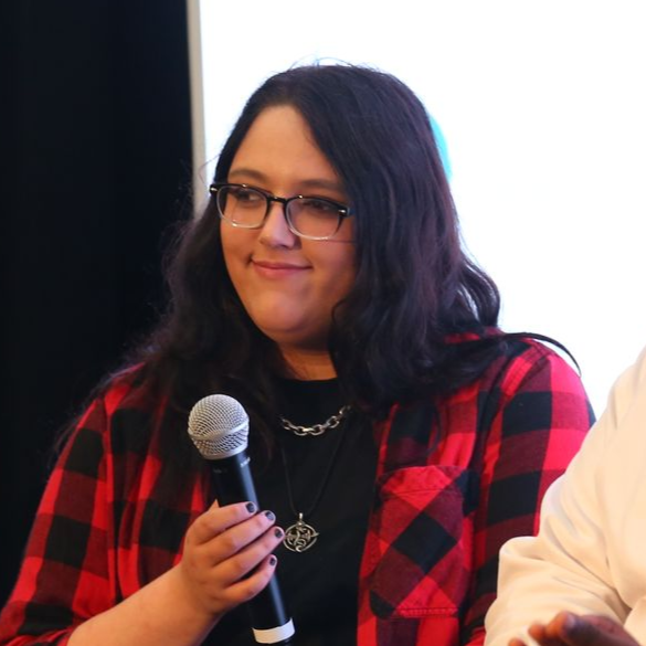 Person in a red plaid shirt holding a microphone and smiling at an indoor event