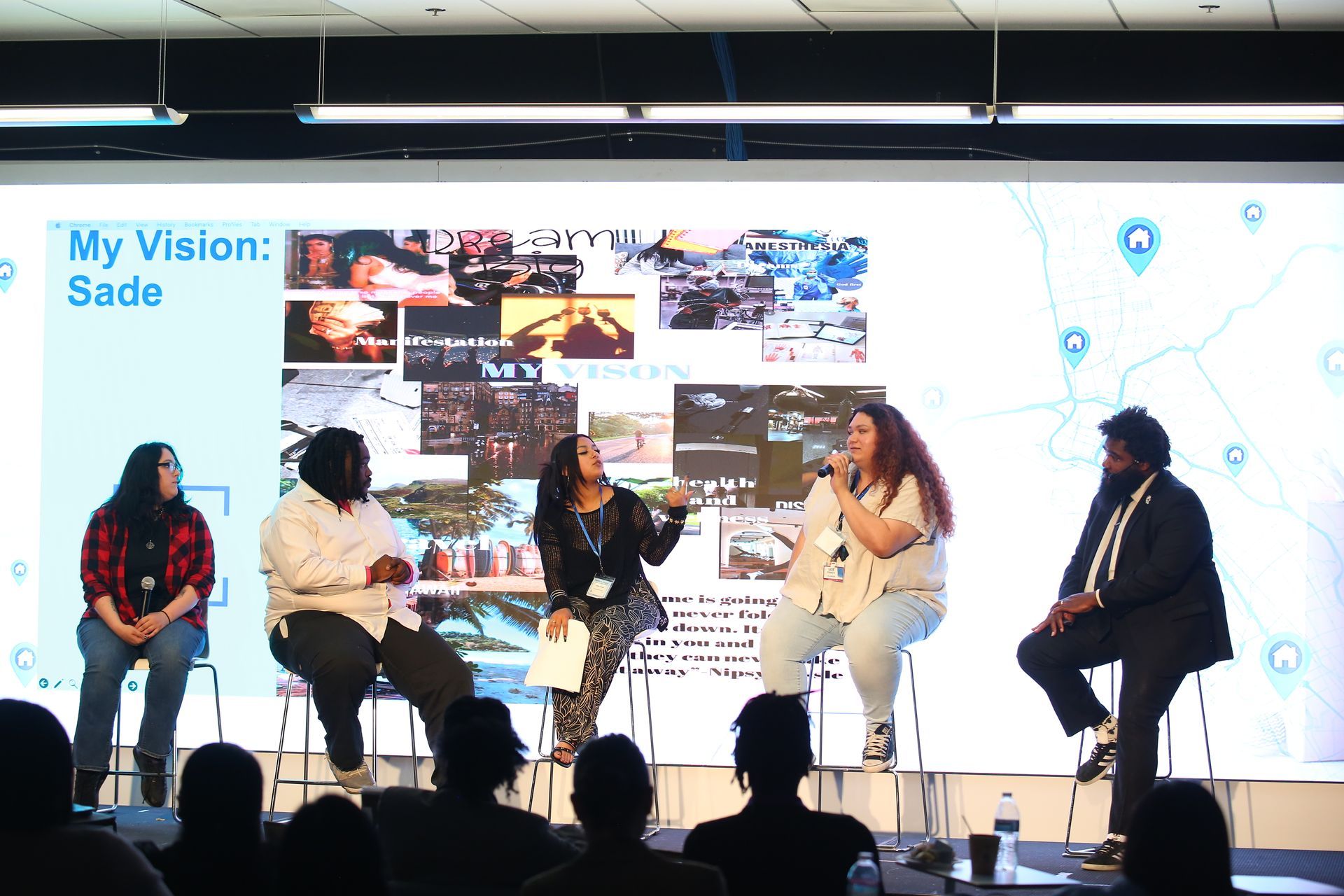 Panel discussion on stage with five speakers seated before a large presentation screen
