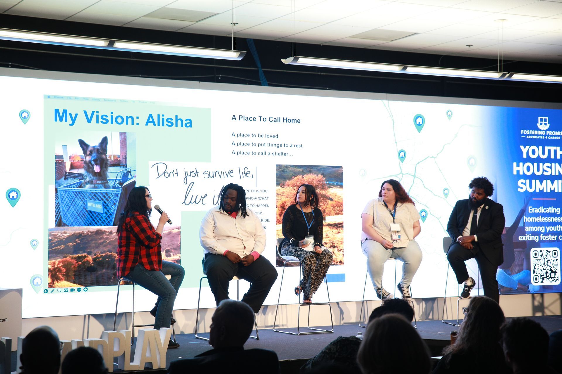 Panel discussion on stage at the Youth Housing Summit, with four speakers seated on stools before a large backdrop.