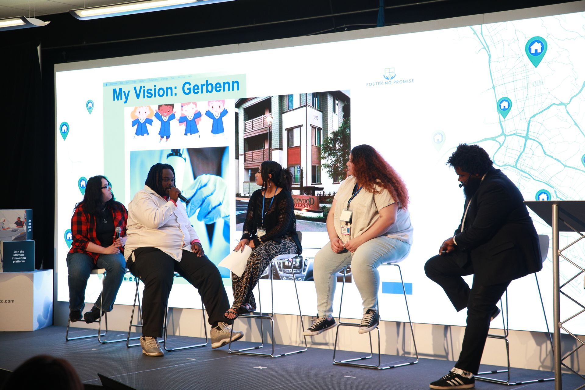Panel discussion on a stage, with four seated speakers and a large screen backdrop behind them.