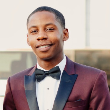 Smiling person in a burgundy tuxedo jacket with black lapels and a bow tie