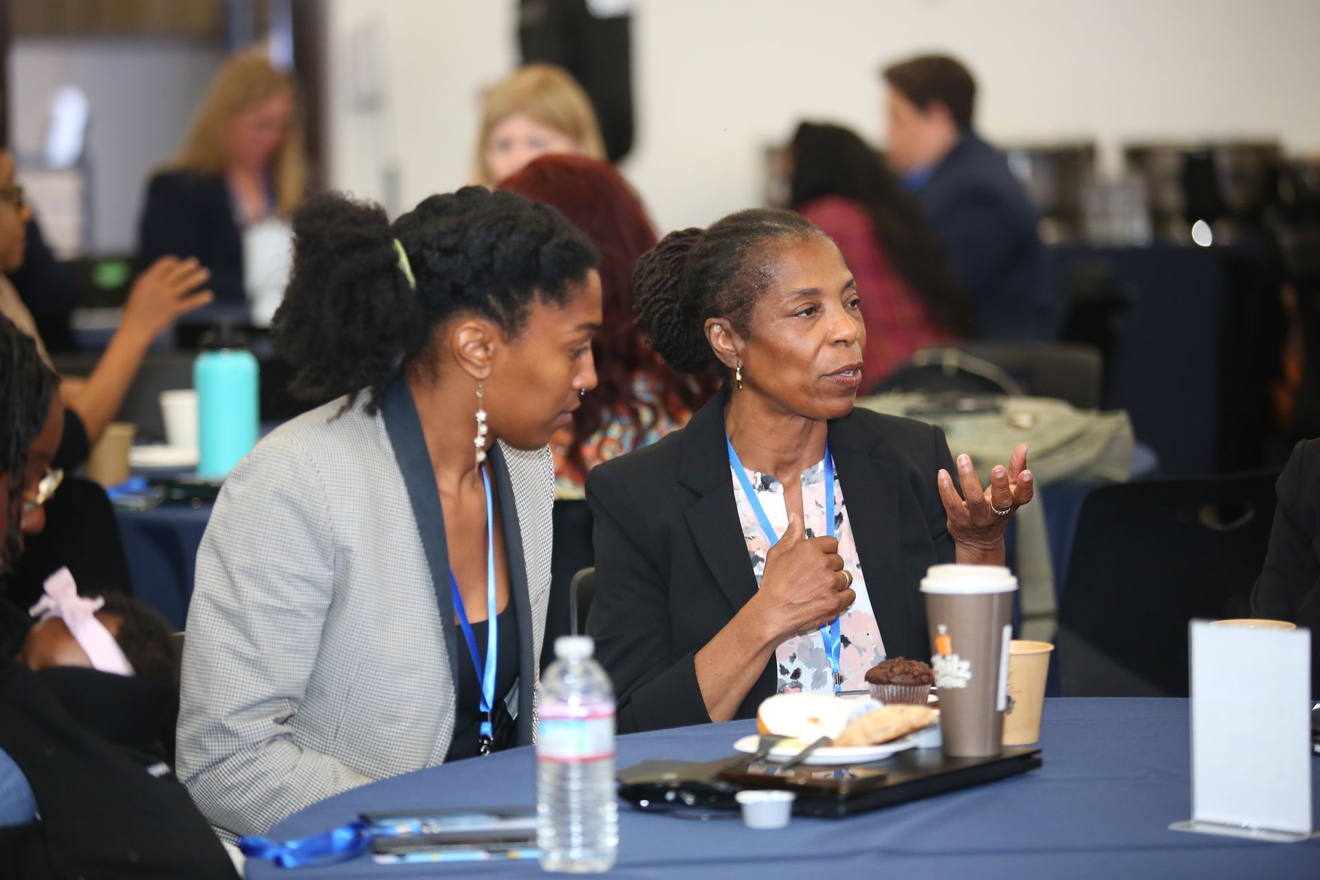 Two people seated at a conference table, talking over coffee in a meeting room.