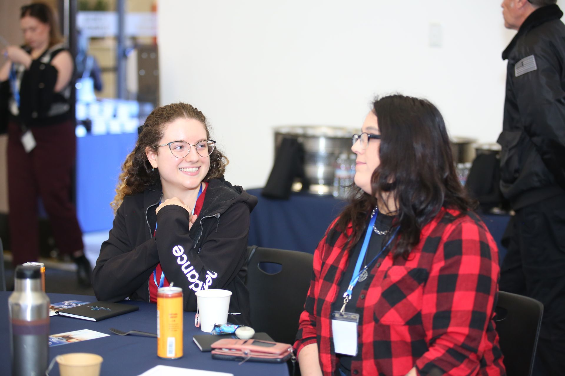 Two people chatting at a table with cups and a notebook in a conference lobby.