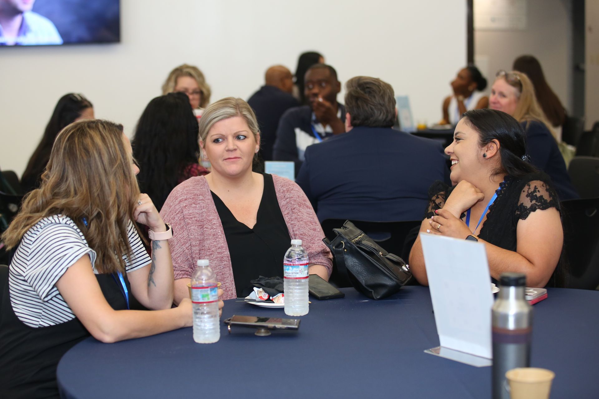 People seated around a table in a meeting room, talking with water bottles and laptops nearby