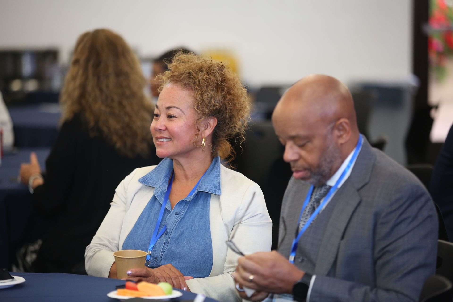 Two people seated at a table, smiling and eating during a casual indoor event
